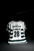 A white and dark green striped soccer jersey with 'BANCO ESPIRITO SANTO', 'C. RONALDO', and the number '28' printed on the back, hanging against a black background.