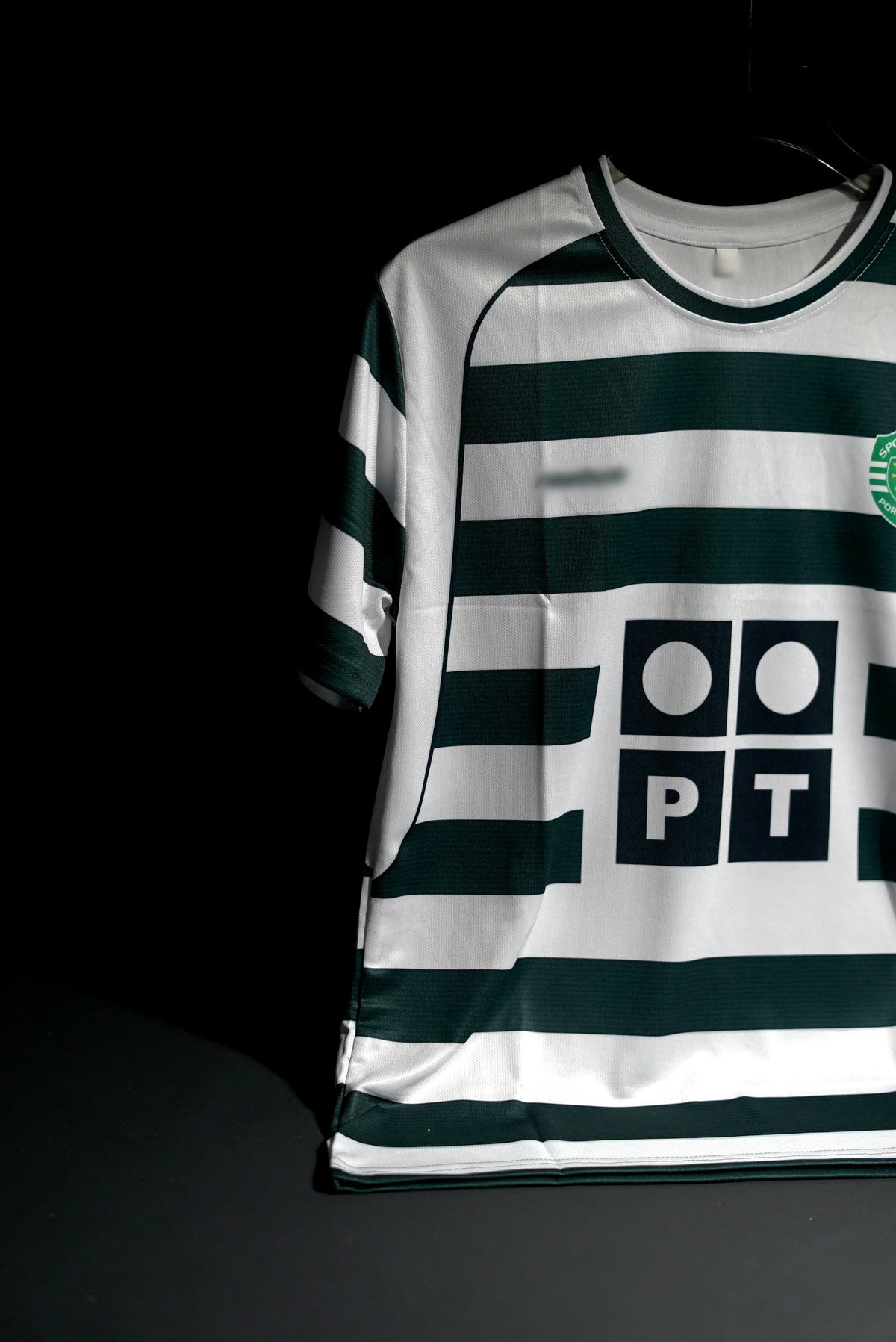 A Sporting Portugal soccer jersey with dark green and white horizontal stripes, featuring the PT logo on the front, displayed against a dark background.